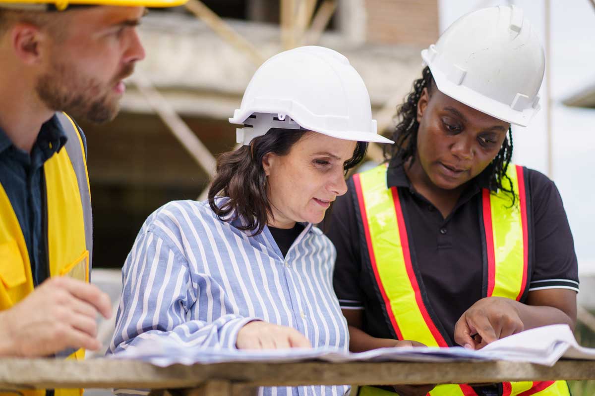 A group of ethnically diverse men and women discuss plans on a building site