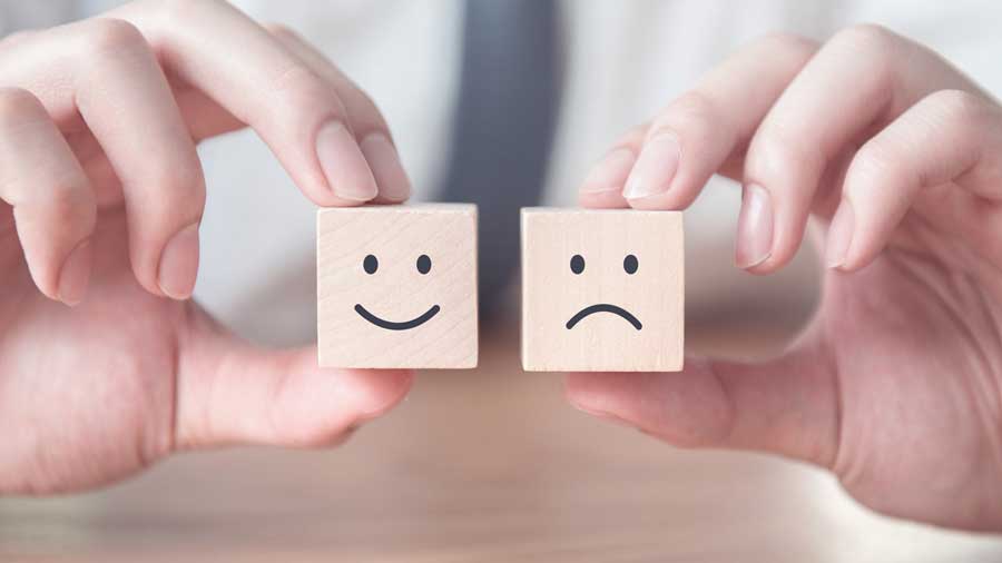 Hands hold wooden cubes with happy and sad faces on them