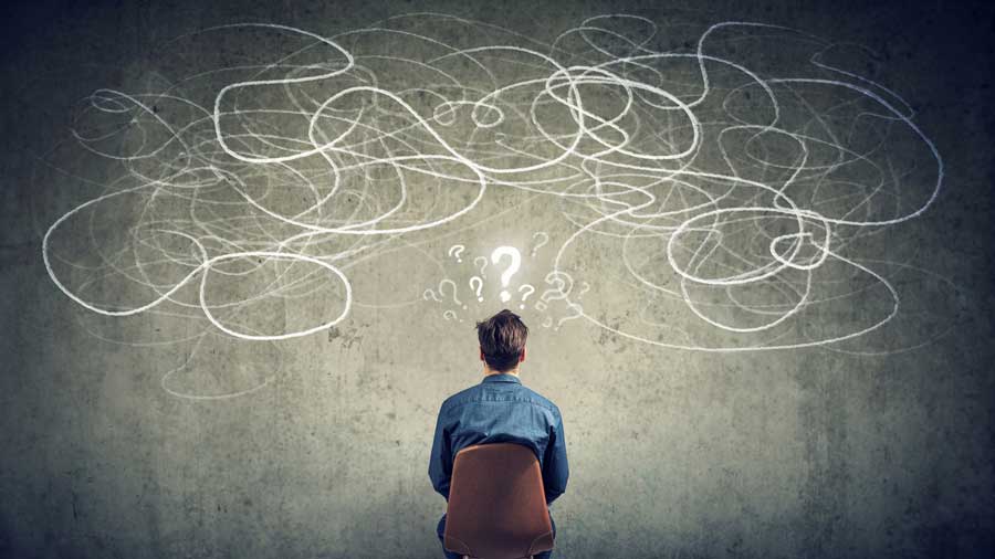 A confused man looks at a wall full of question marks