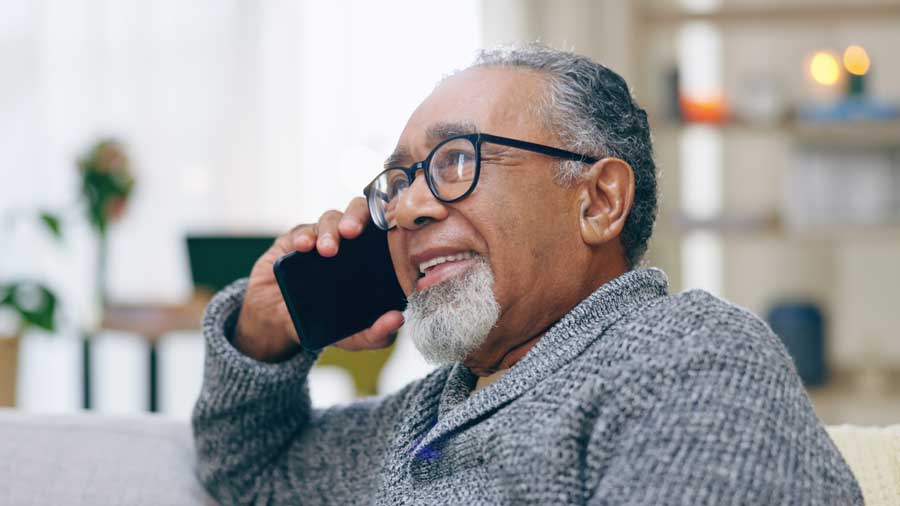 An older man smiles while talking on the phone