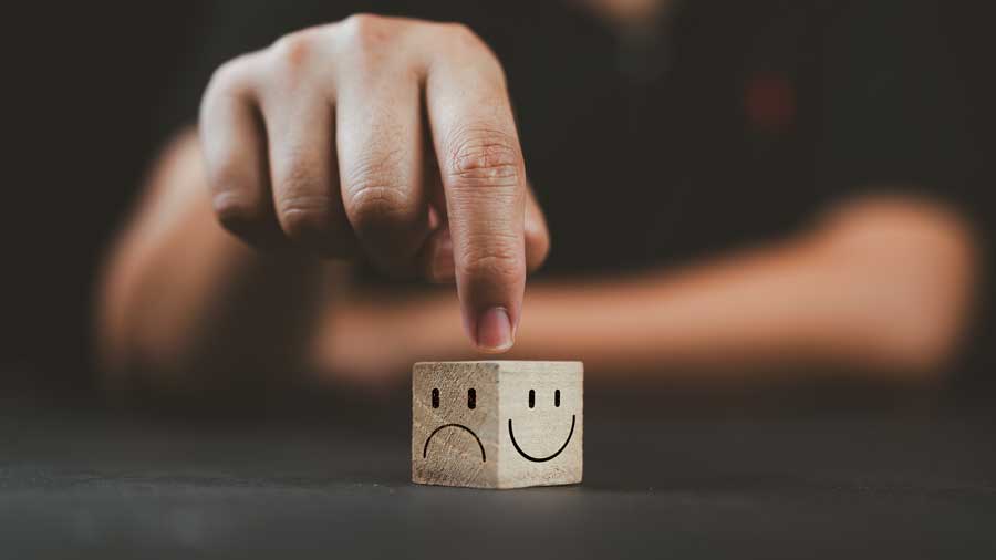 A hand points at a wooden cube with a happy face on one side and a sad face on the other