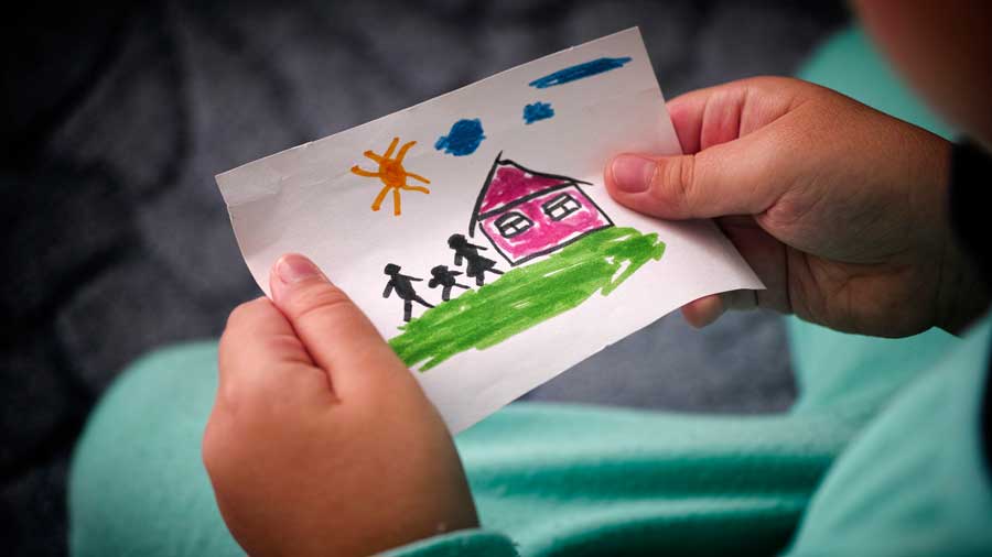 A child holds a colourful drawing of a house