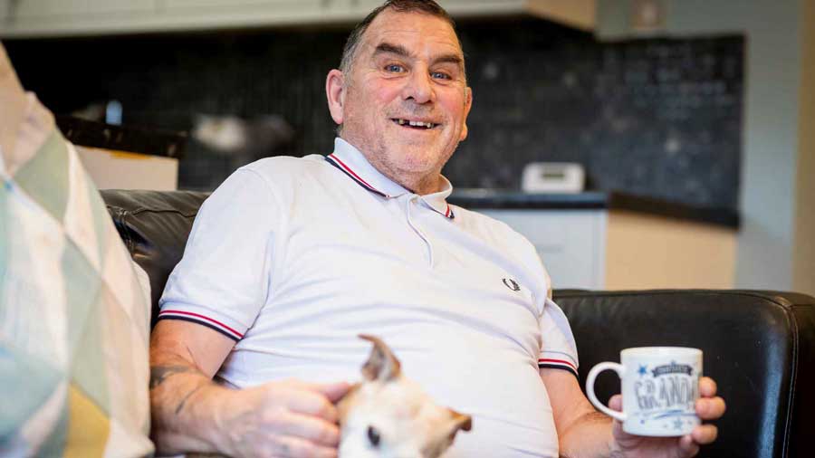 Older man sits on his sofa with his pet dog