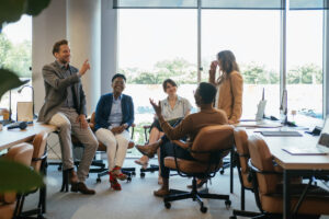 Team of five multi-ethnic employee having fun working together in an open plan office with big windows.