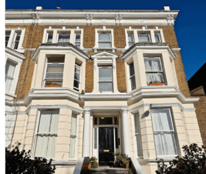 A large Victorian-era home. Three story building with bay windows and a black front door.
