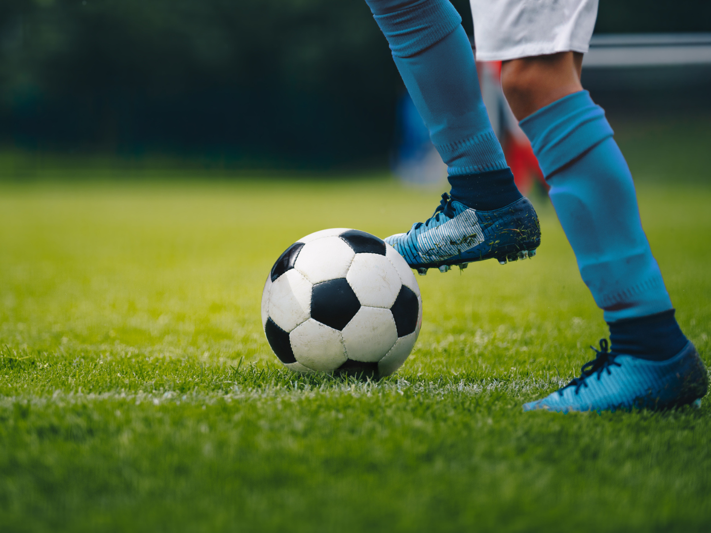 Close up of legs and feet of football player in blue socks and shoes running and dribbling with the ball. Soccer player running after the ball. Sports venue in the background