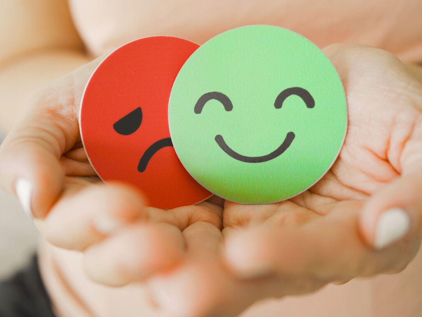 Pair of hands holding two cardboard faces. One is red and sad. The other is green and happy.