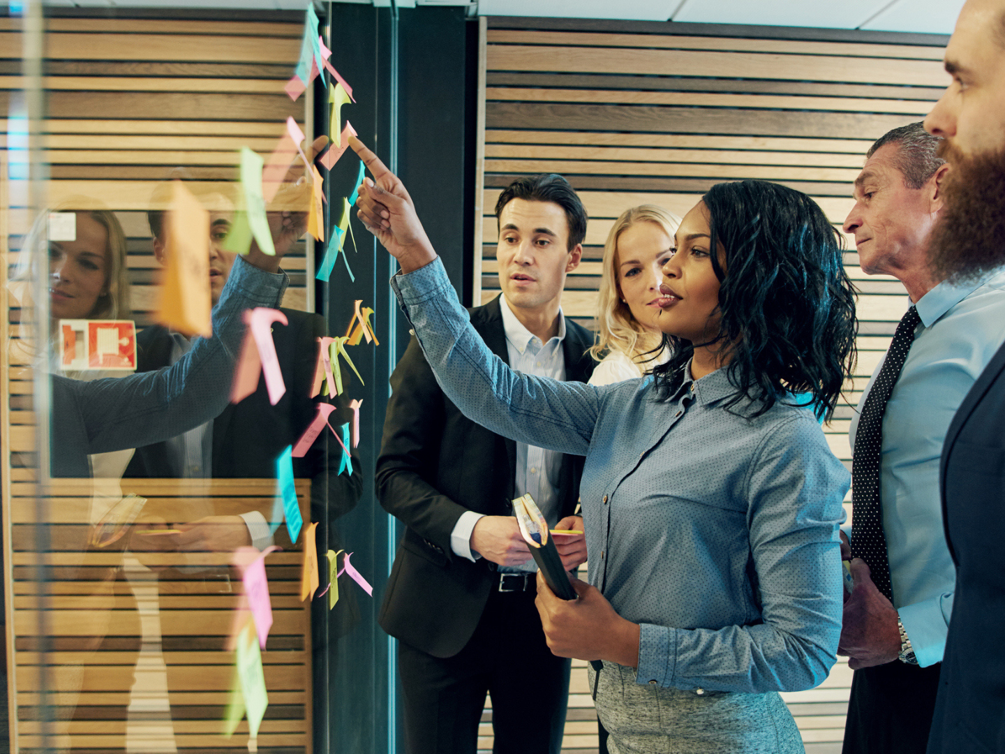 A business woman placing post-it notes on a board as colleagues watch.
